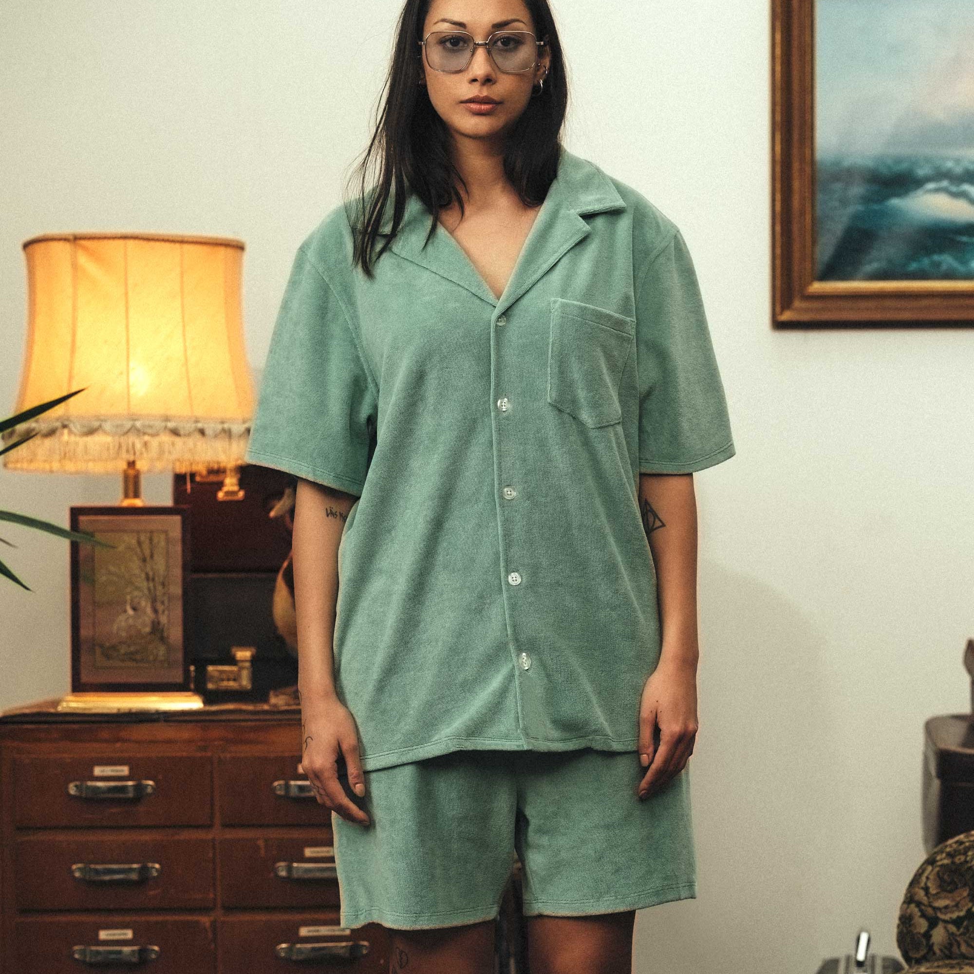 Female model wearing a grey-green short sleeve shirt with white button closure and one chest pocket