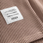 Close-up on a stitched-on material label on a brown waffle-patterned sweatshirt.