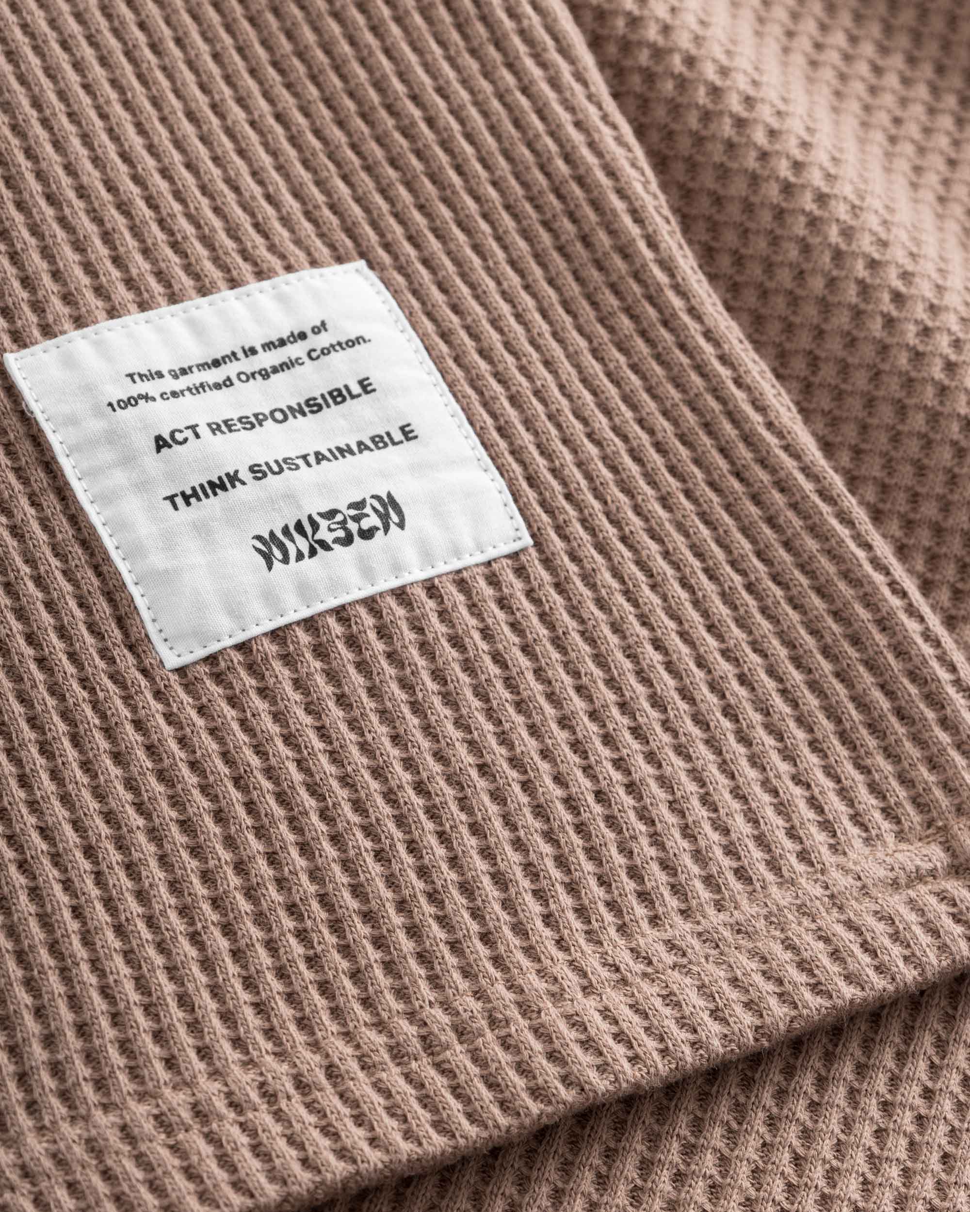 Close-up on a stitched-on material label on a brown waffle-patterned sweatshirt.