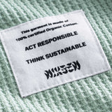 Close-up on a stitched-on material label on a mint green waffle-patterned sweatshirt.