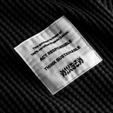 Close-up on a stitched-on material label on a black waffle-patterned sweatshirt.