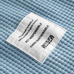 Close-up on a stitched-on material label on a sky blue waffle-patterned sweatshirt.