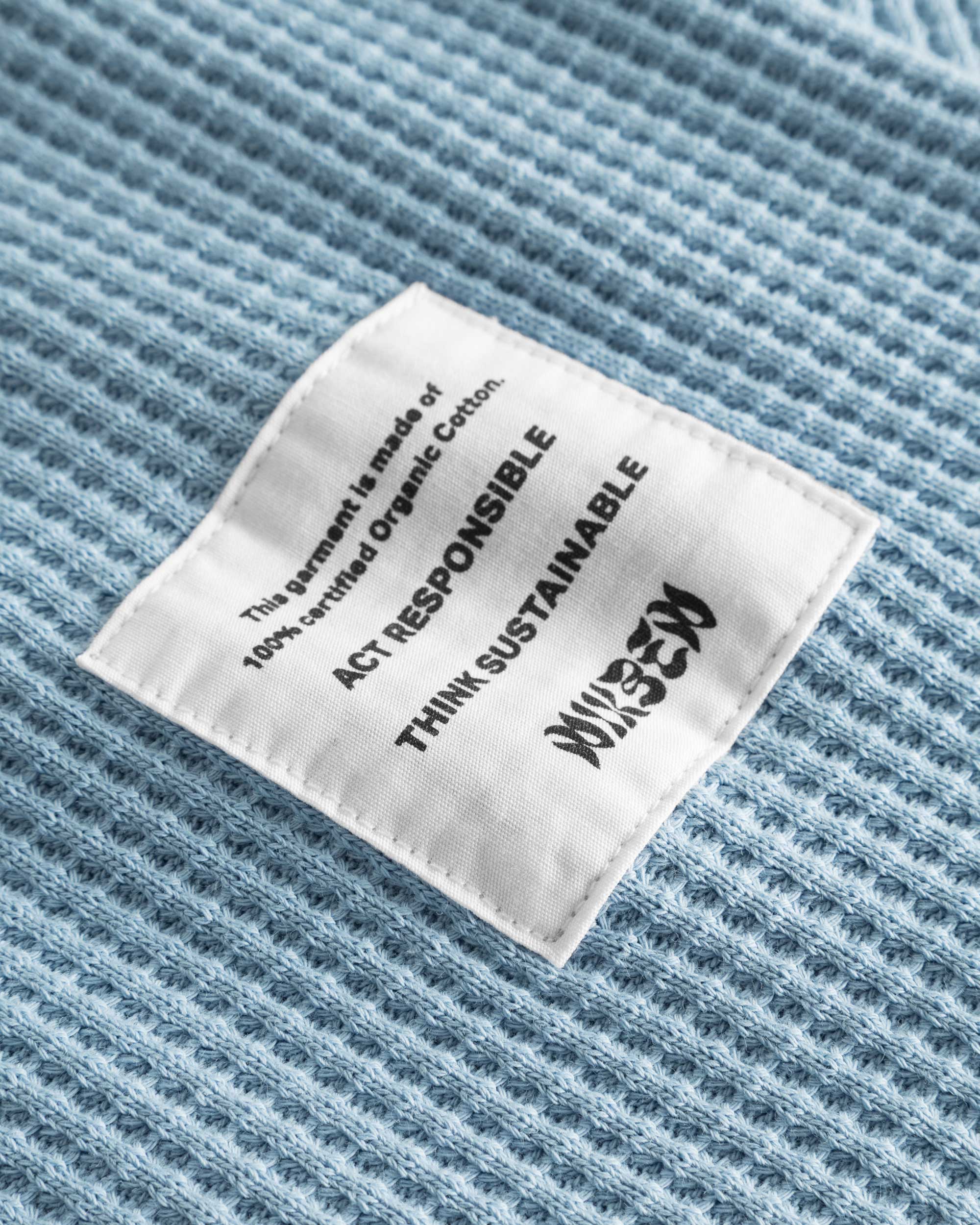 Close-up on a stitched-on material label on a sky blue waffle-patterned sweatshirt.