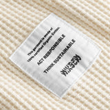 Close-up on a stitched-on material label on an off white waffle-patterned sweatshirt.