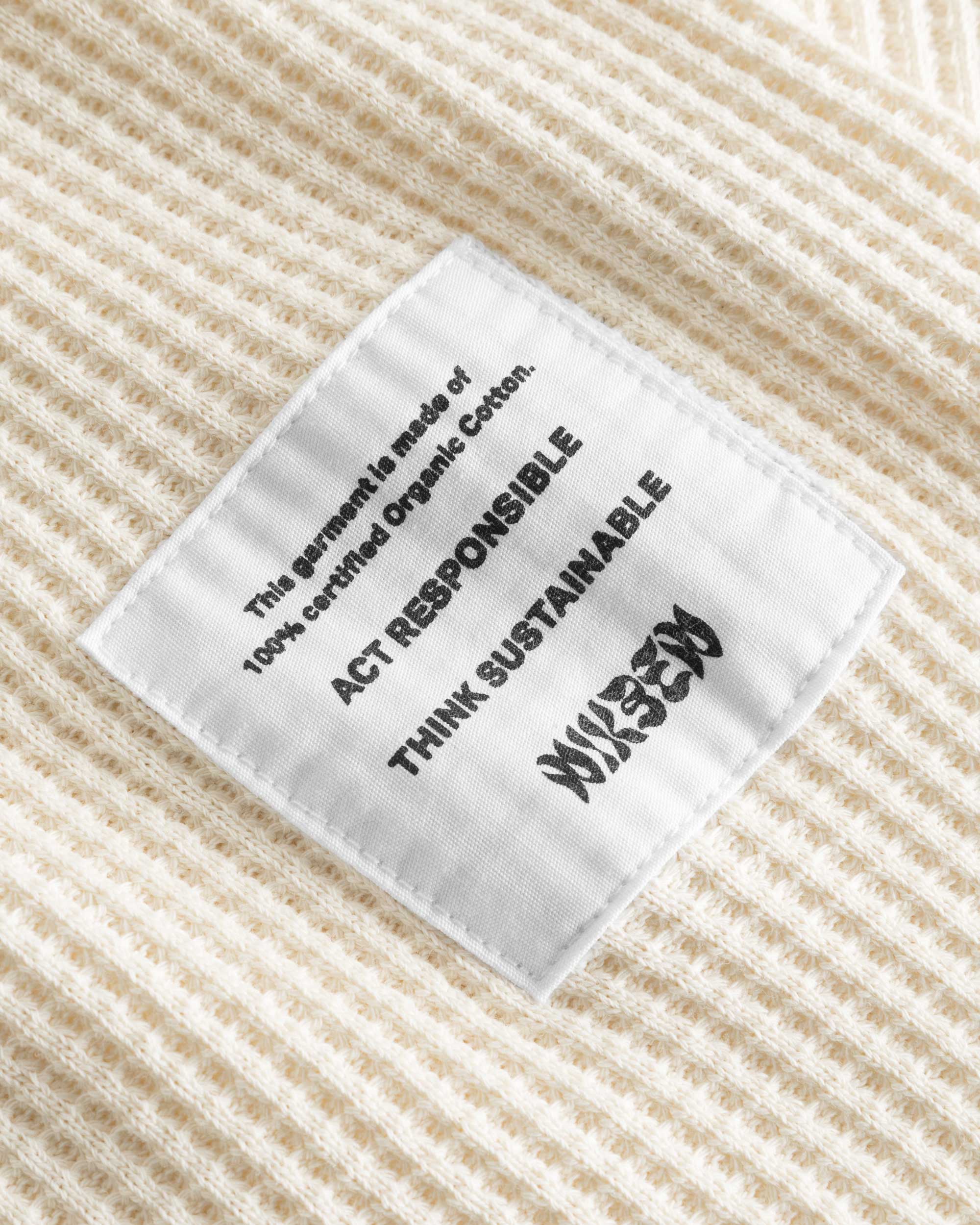 Close-up on a stitched-on material label on an off white waffle-patterned sweatshirt.