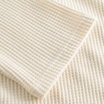 Close up on stitchings and sleeve on an off white waffle-patterned sweatshirt