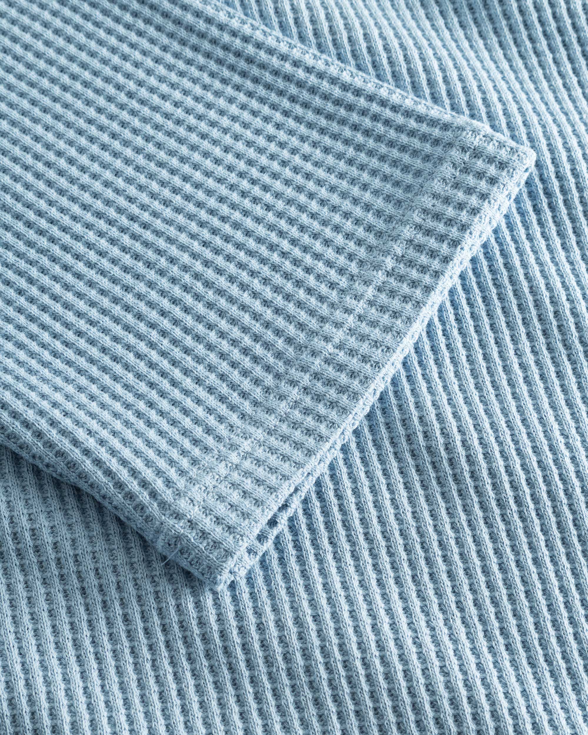 Close up on stitchings and sleeve on a sky blue waffle-patterned cropped sweatshirt