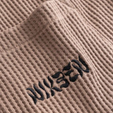 Close-up view of front pocket with stitched black logo on a brown waffle-patterned shirt