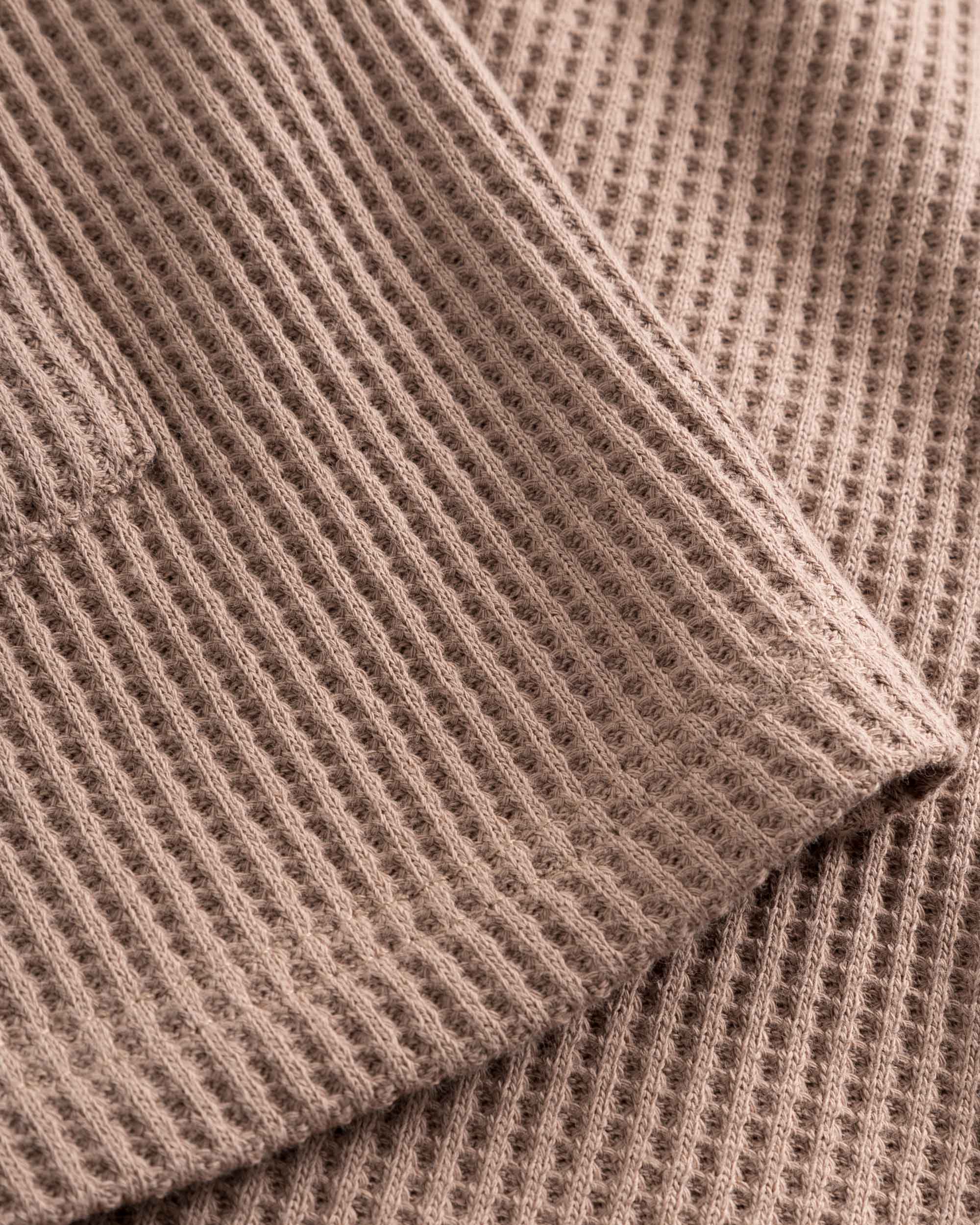 Close-up of stitchings and sleeve on a brown waffle-patterned shirt.