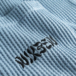 Close-up view of front pocket with stitched black logo on a sky blue waffle-patterned shirt