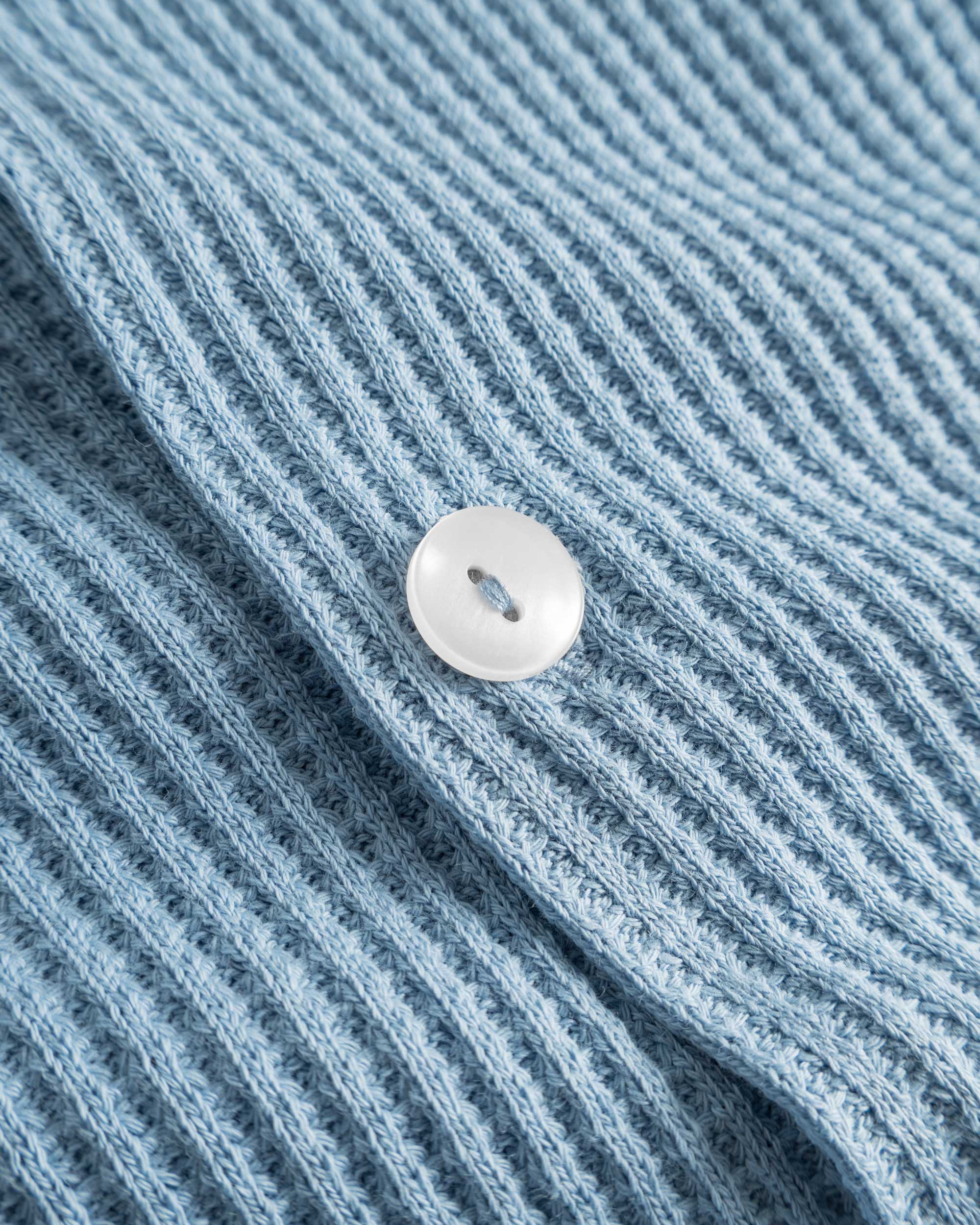 Close-up of pearl button on a sky blue waffle-patterned shirt.