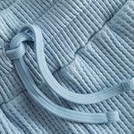 Close up of drawstring on sky blue waffle-patterned short-length shorts.