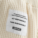 Close up of stitched on material label on off white waffle-patterned short-length shorts.
