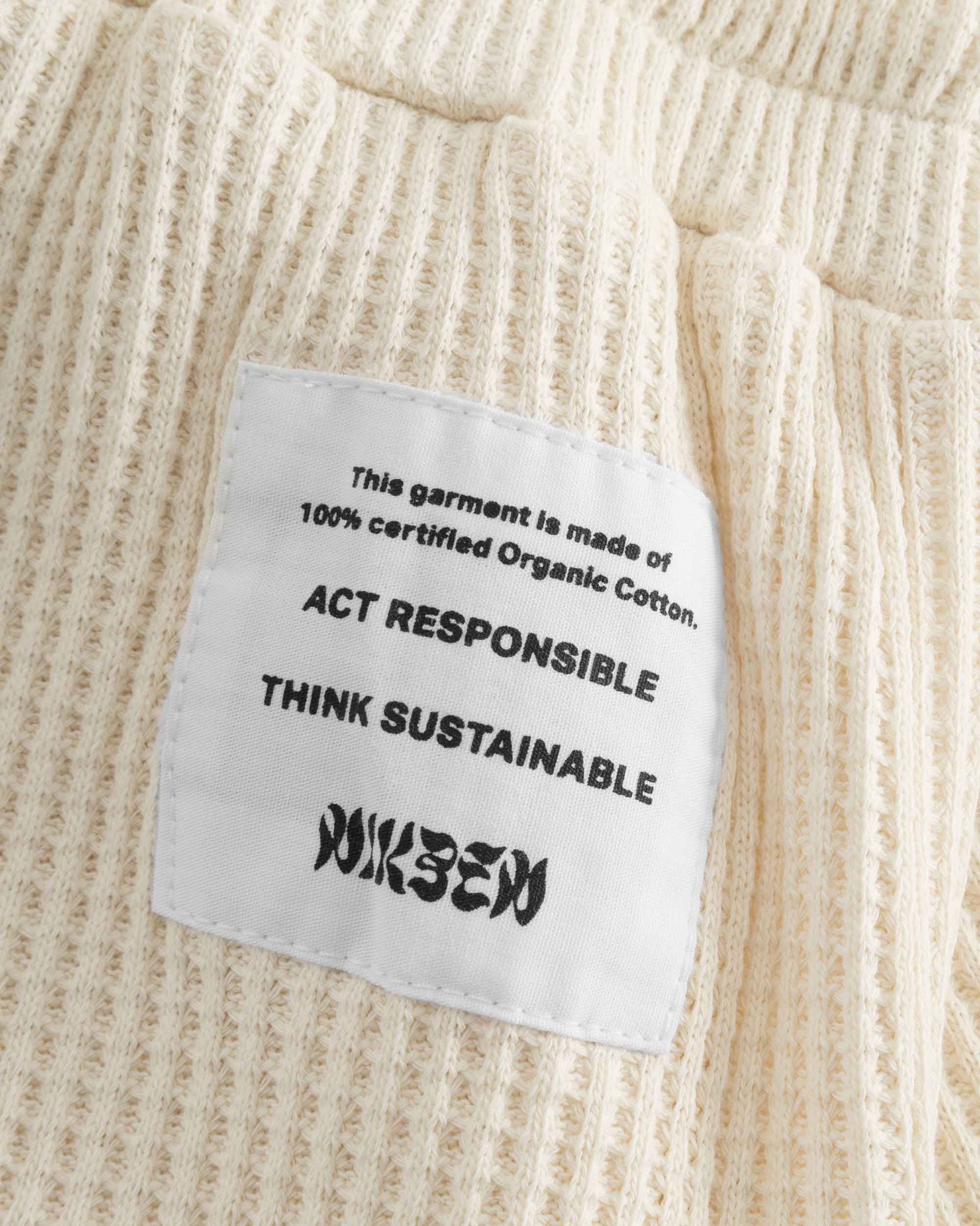 Close up of stitched on material label on off white waffle-patterned short-length shorts.