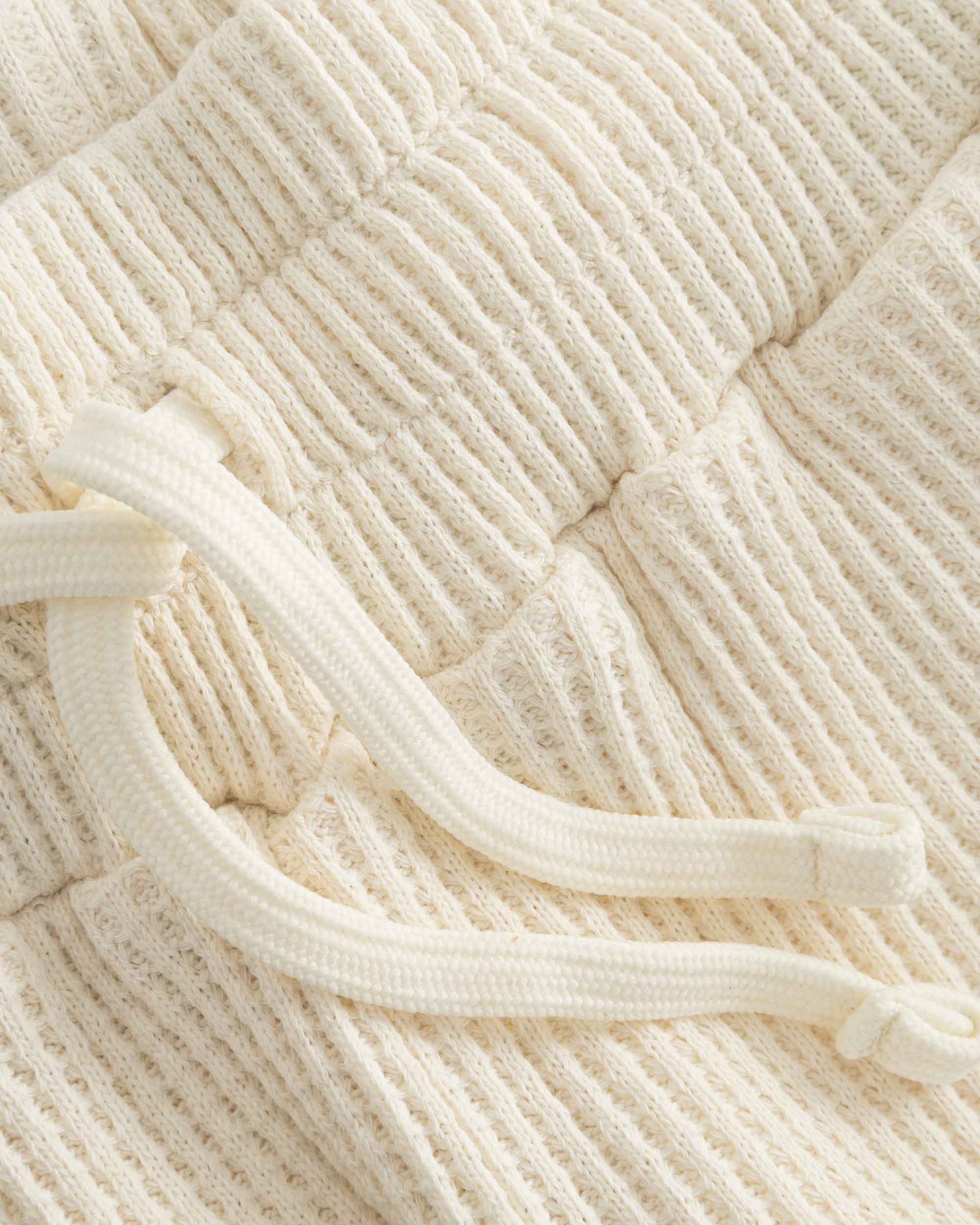 Close up of drawstring on off white waffle-patterned short-length shorts.