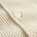 Close-up of pearl button on an off white waffle-patterned shirt.