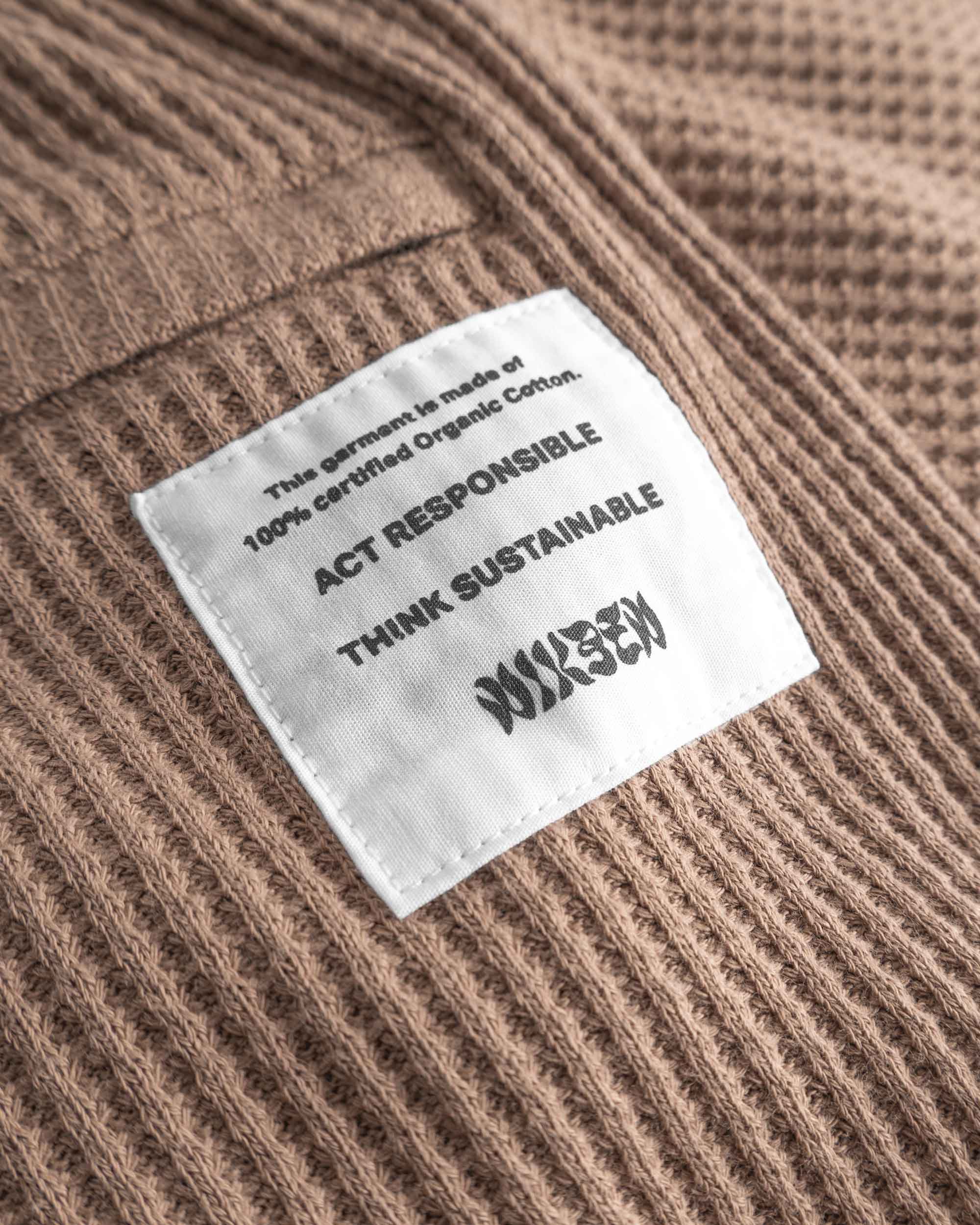 Close up of back pocket and stitched on material label on brown waffle-patterned mid-length shorts.