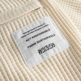 Close up of back pocket and stitched on material label on off white waffle-patterned mid-length shorts.