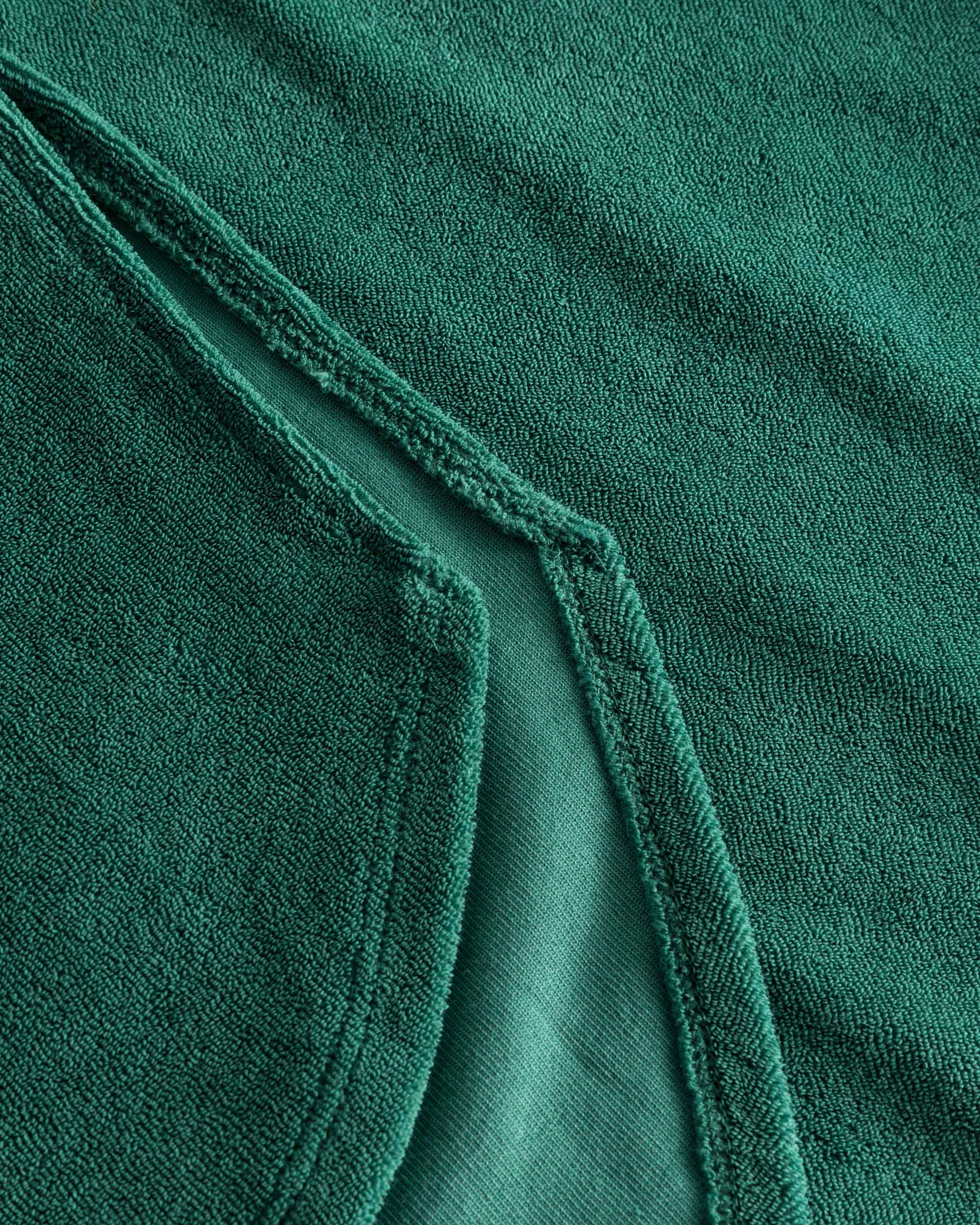 Close up on stitchings on a green kaftan in terry toweling fabric.