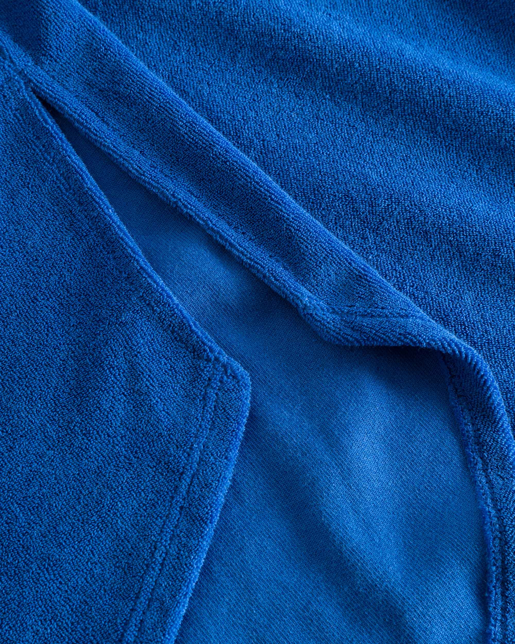 Close up on stitchings on a blue kaftan in terry toweling fabric.