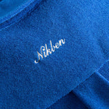 Close up on embroidered logo on a blue kaftan in terry toweling fabric.