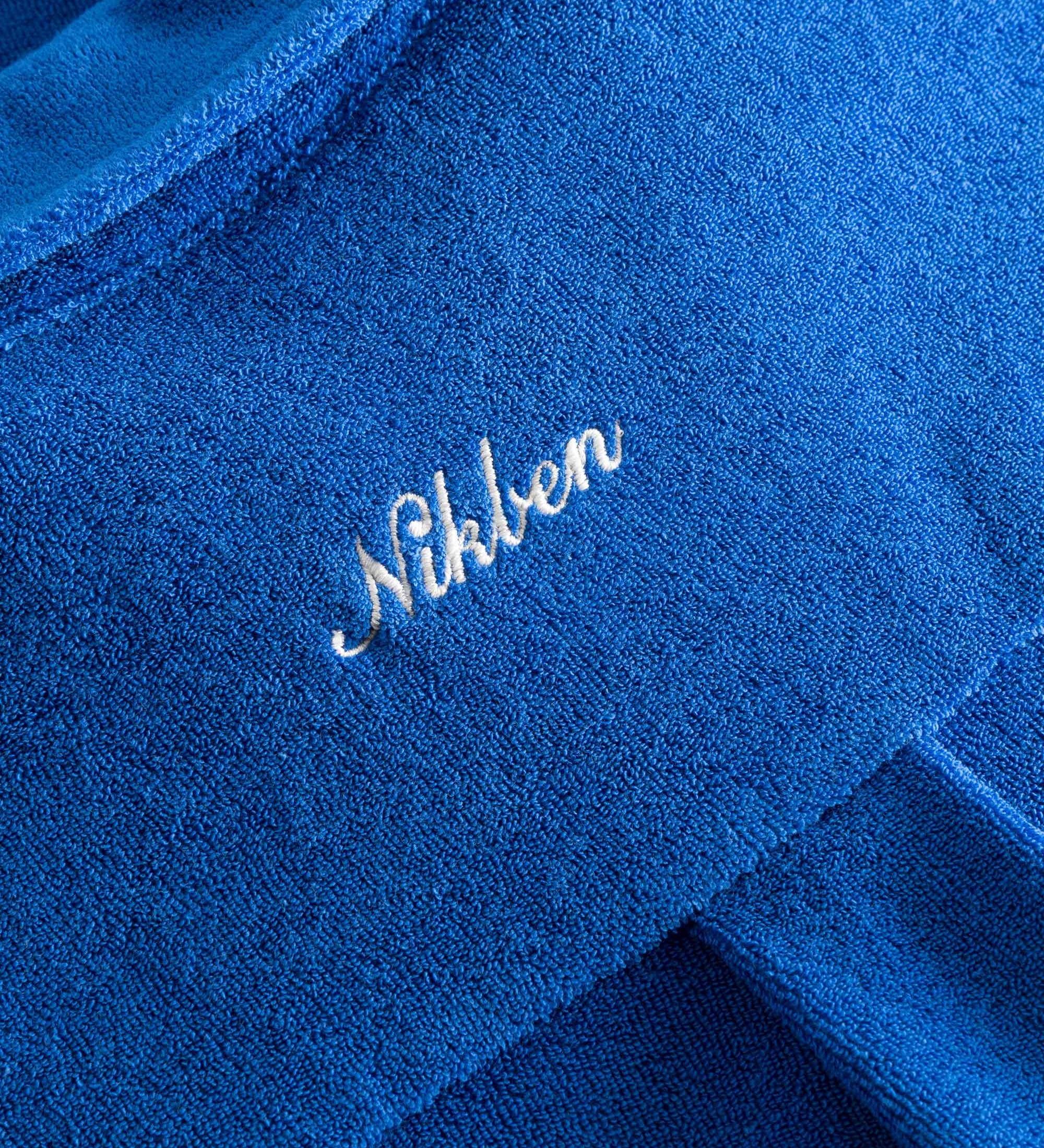 Close up on embroidered logo on a blue kaftan in terry toweling fabric.